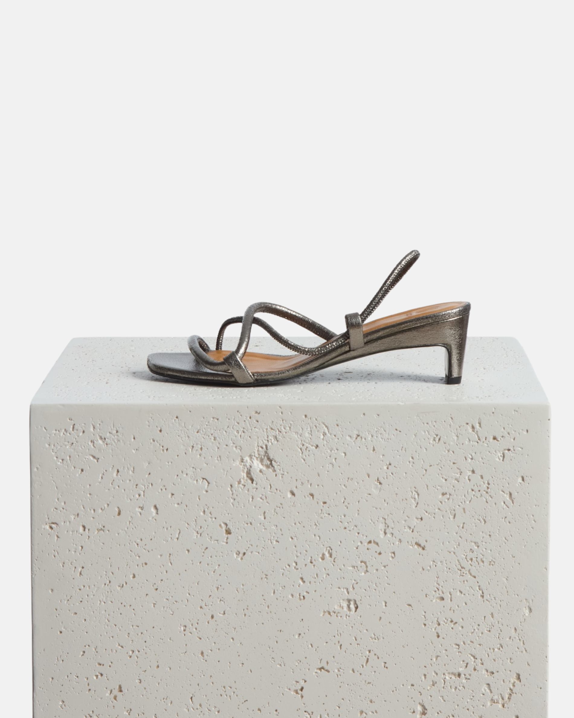 Shoe on a plinth: metallic pewter leather mid-heel sandal with slim crossover straps, an elastic slingback, and a softly contoured demi heel.