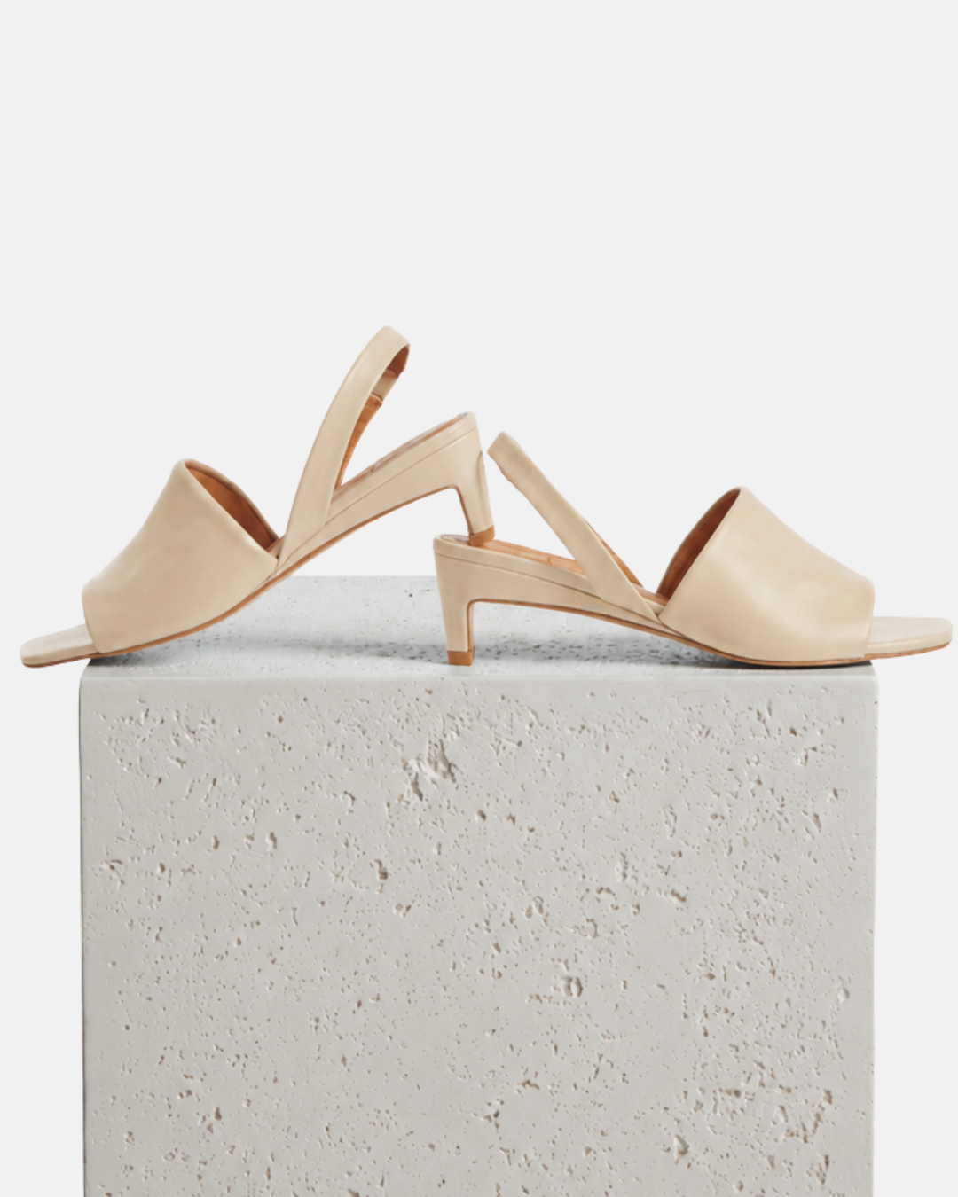 Pair of off-white slingback mid-heeled sandals on a stone pedestal against a light grey background