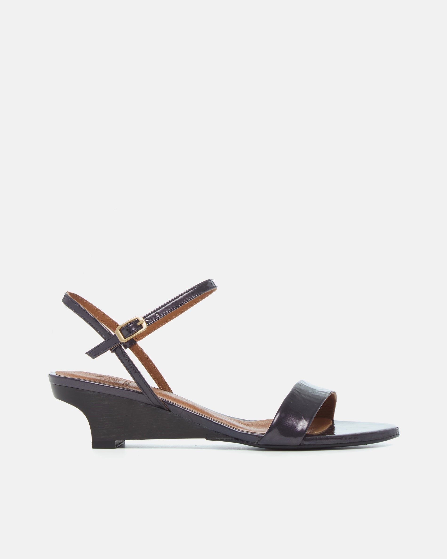 Side view of a black pearl patent leather sandal with a slim strap, ankle buckle, and sculptural wooden demi-wedge