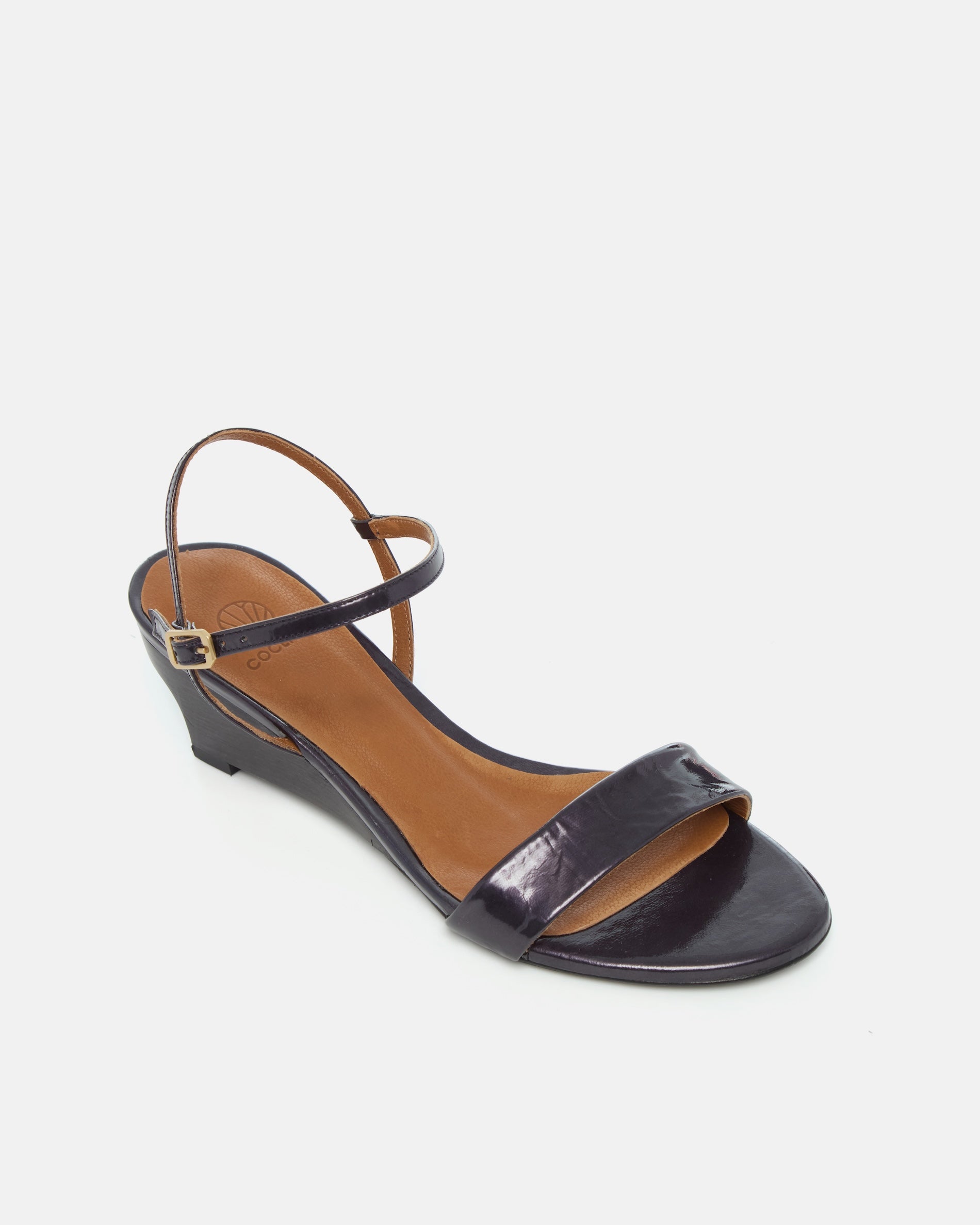 Angled view of a black pearl patent leather sandal with a slim strap, ankle buckle, and sculptural wooden demi-wedge
