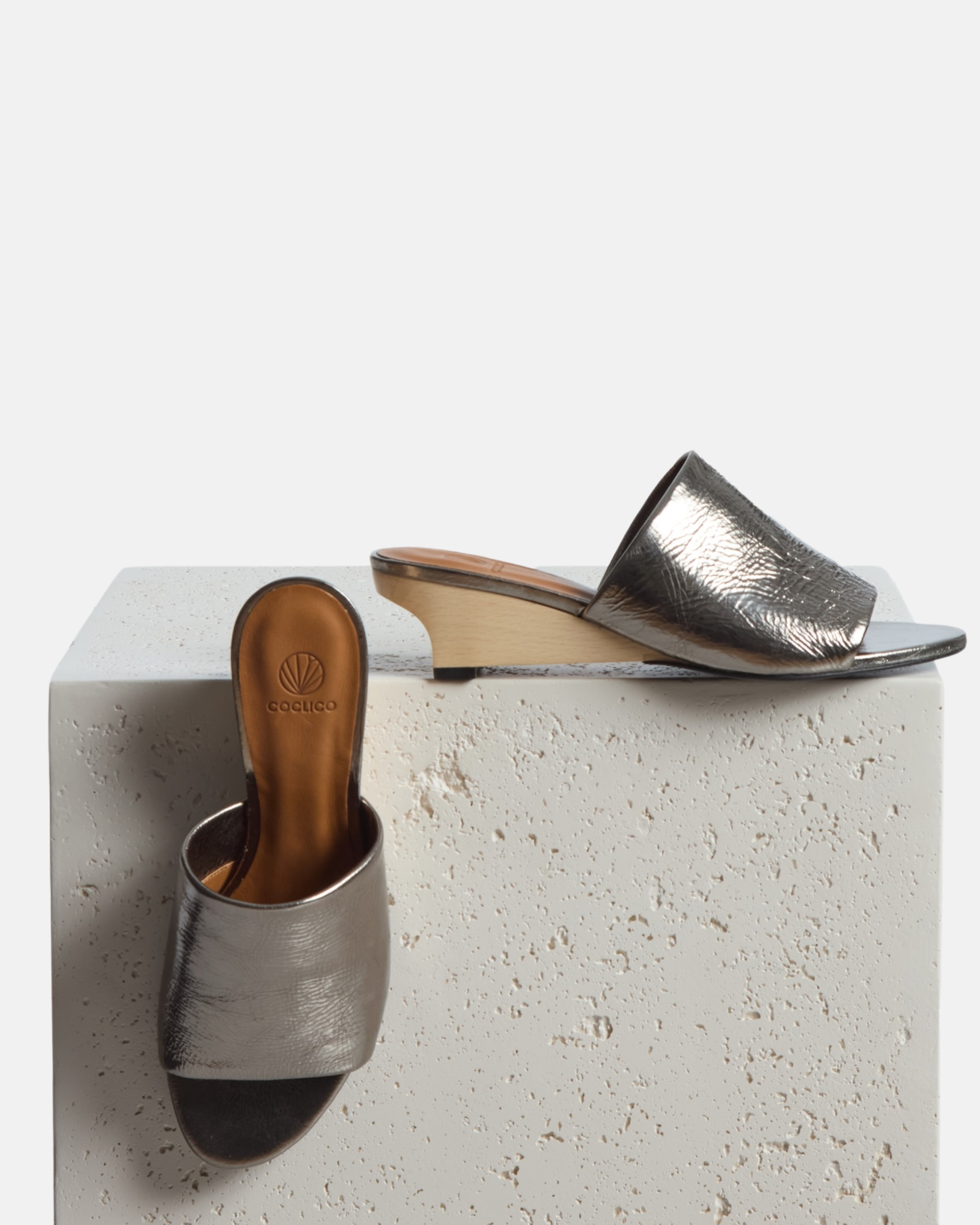 Shoes on a plinth: pewter metallic slide sandal with a wide crinkled leather band and sculptural wooden demi-wedge