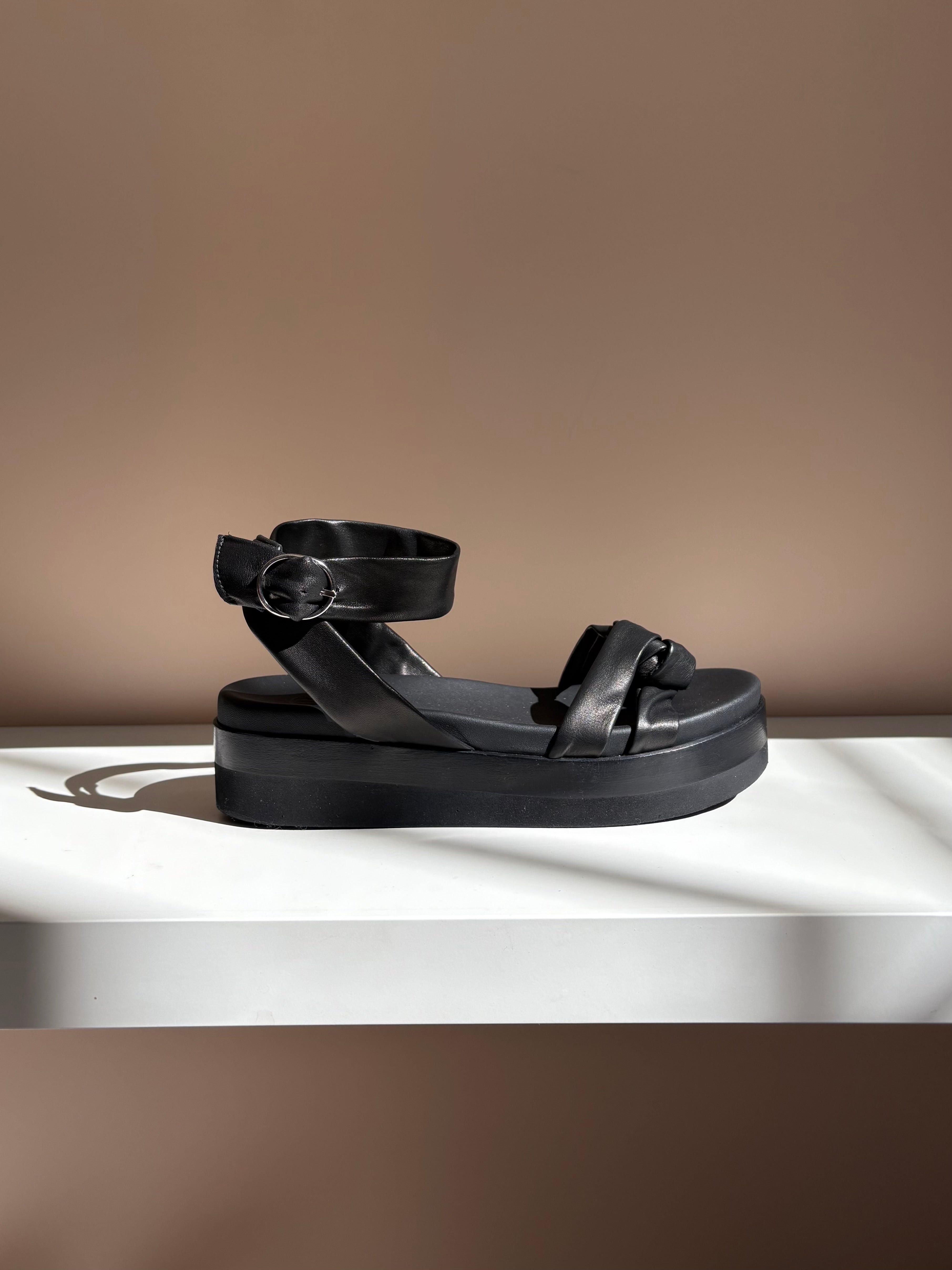 Black sandals with thick, cushioned soles, featuring wide straps and silver buckle accents, crafted from smooth leather with a matte finish.