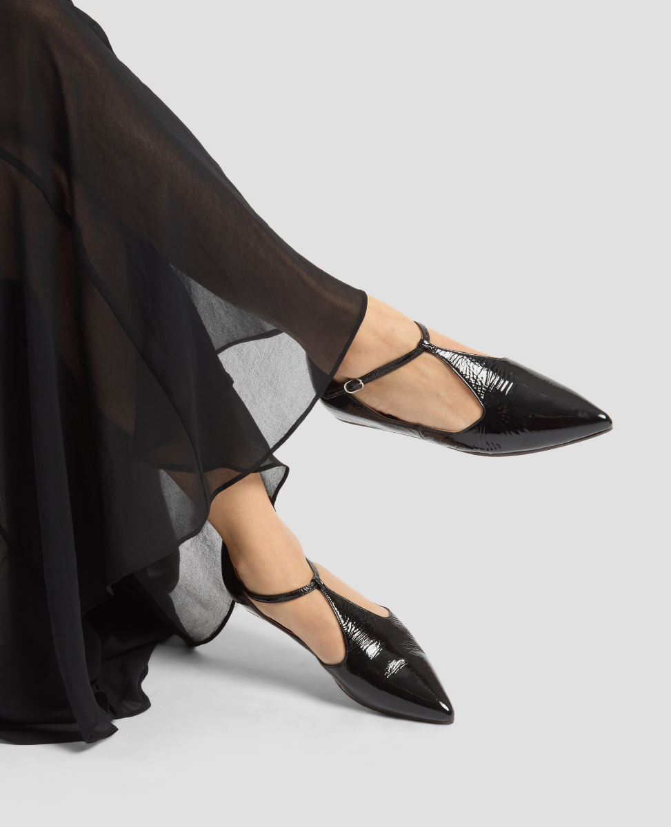 Black pointed-toe flats worn with a long black skirt on a light gray background