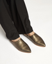 Pointed-toe, slip-on shoes with a metallic bronze finish, smooth leather texture, and a flat sole, worn with black pants. 3