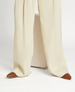 Cream-colored, wide-leg pants with a smooth texture, made from a lightweight fabric, featuring brown leather toe caps on the shoes visible beneath the hem. 2