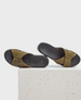 A pair of olive green leather sandals with crisscross straps, a smooth black footbed, and a minimalist design, resting on a textured white surface. 1