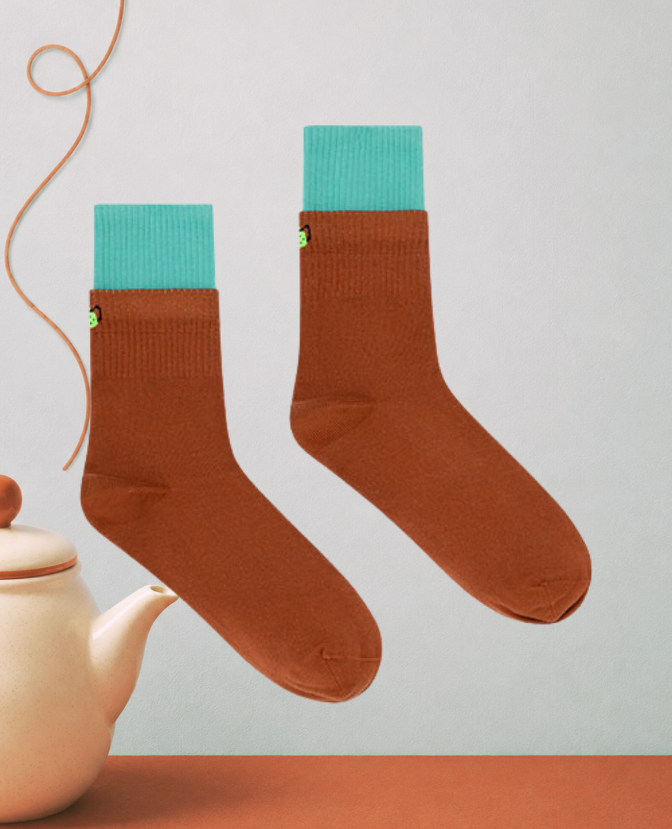 Dr Bloom Teapot Socks in Brown, rust cotton crew socks with a contrast teal folded cuff, styled beside a cream teapot