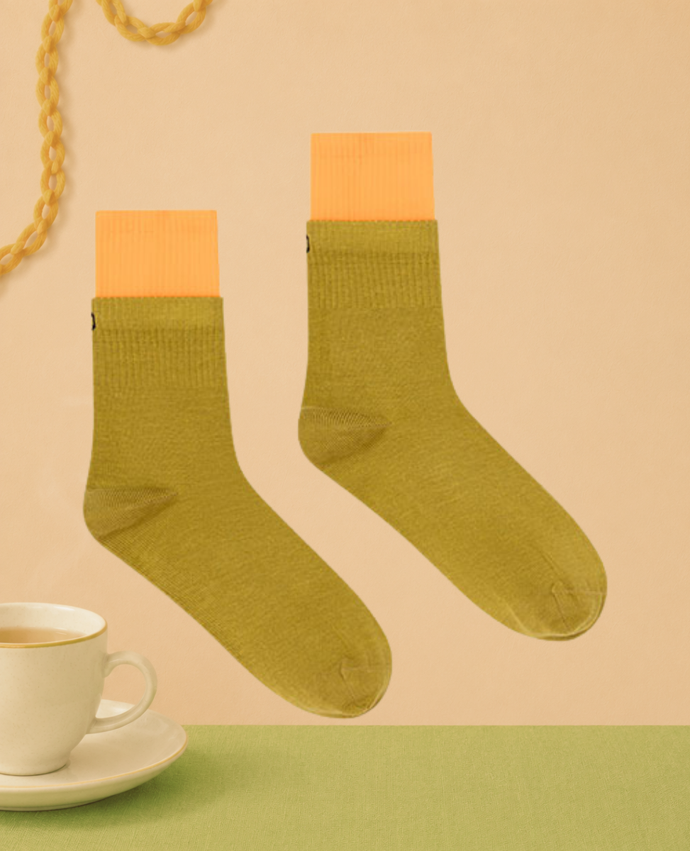 Dr Bloom Teapot Socks in Ochre, olive green cotton crew socks with a contrast orange folded cuff, styled with a cup of tea