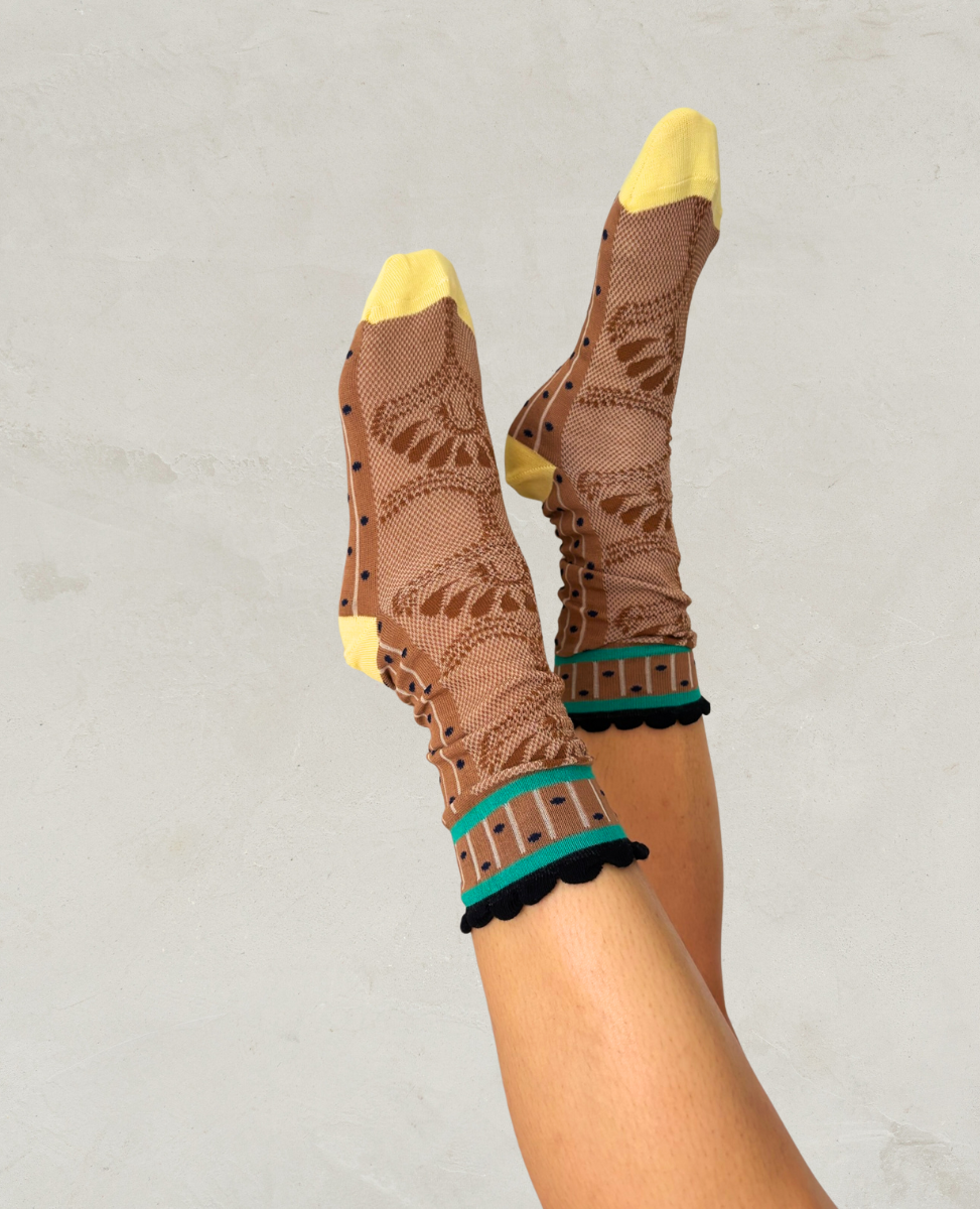 Brown patterned socks with yellow toes and black cuffs on a light gray background