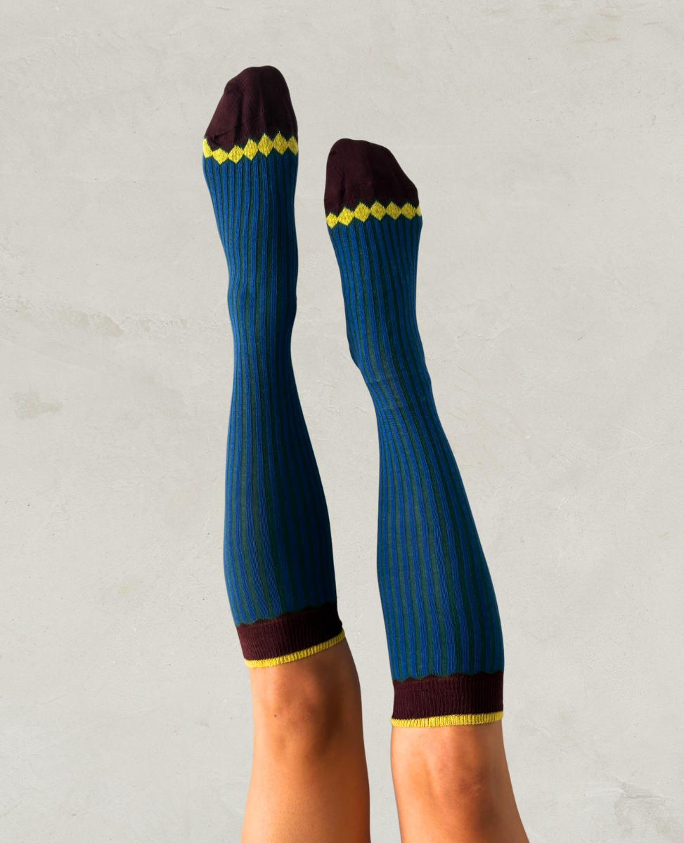 Blue knee-high socks with yellow and maroon accents worn by a person on a light gray background