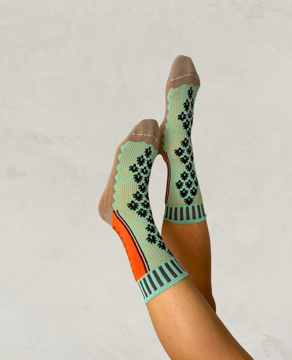 Person wearing mint green socks with black pattern and orange accents on a plain background