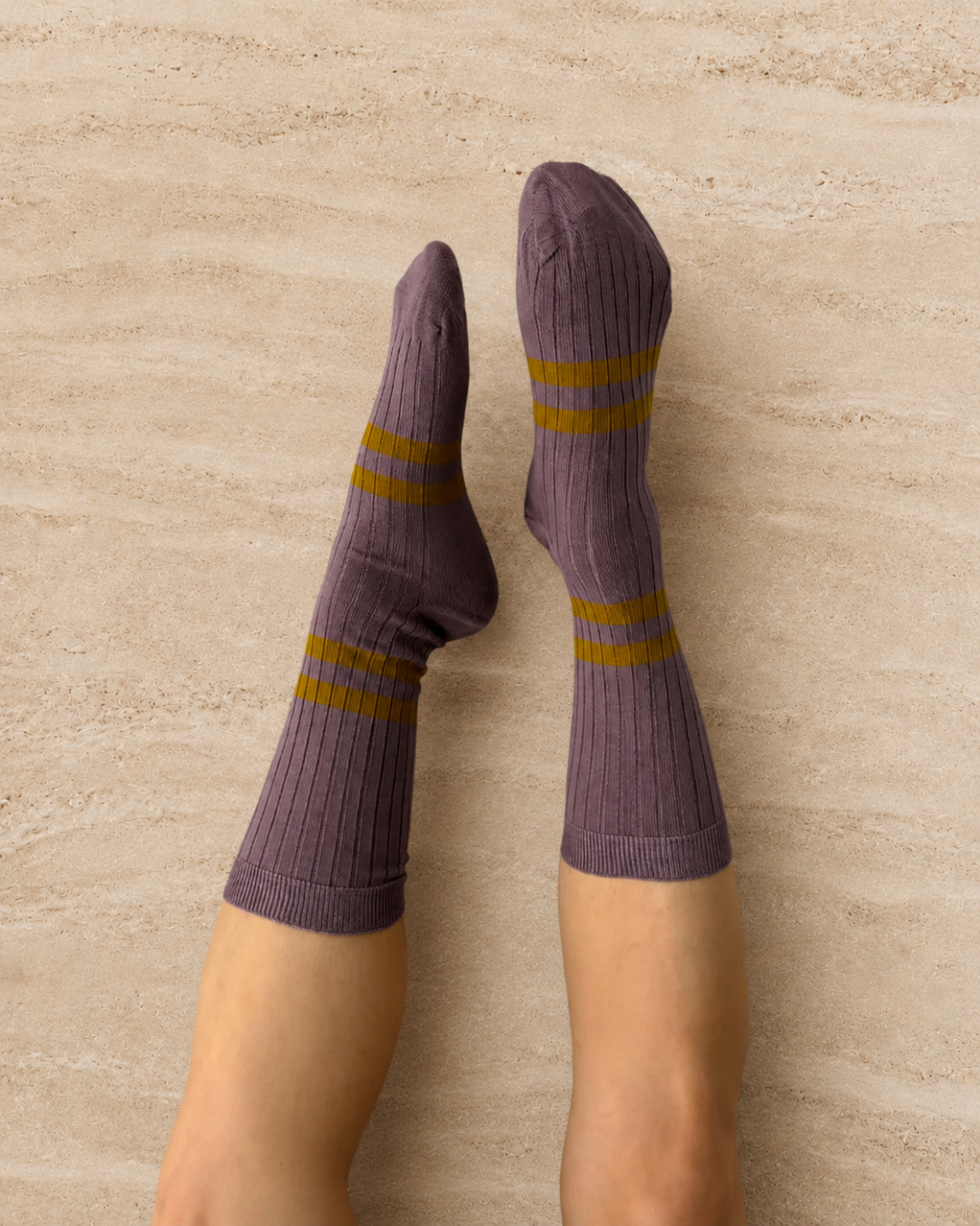Escuyer Purple socks with yellow stripes worn by a person on a light gray background