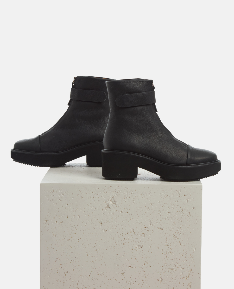 Black ankle boots on a light gray pedestal against a white background