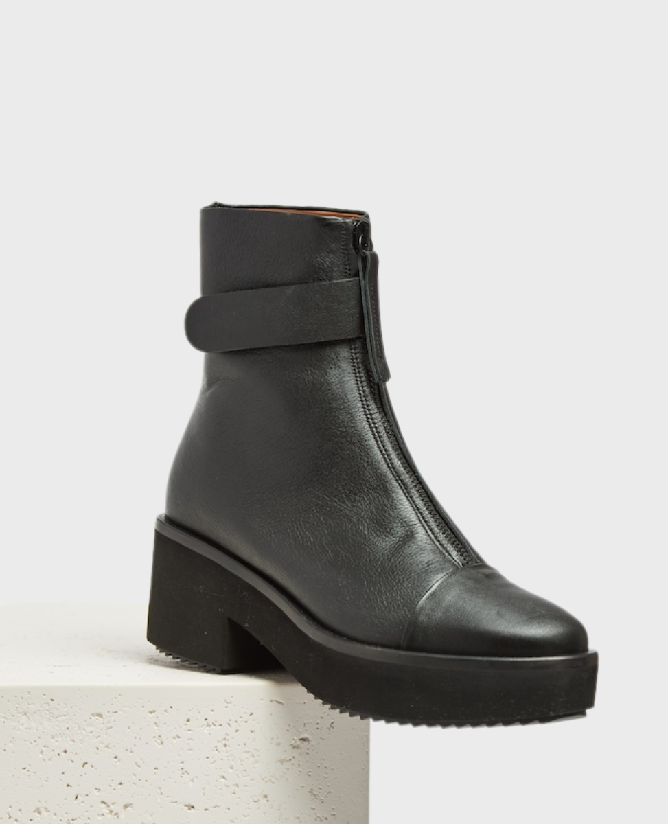 A black leather ankle boot with a front zipper, a strap detail around the ankle, a chunky platform heel, and a textured rubber sole.