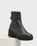 A black leather ankle boot with a front zipper, a strap detail around the ankle, a chunky platform heel, and a textured rubber sole. 1