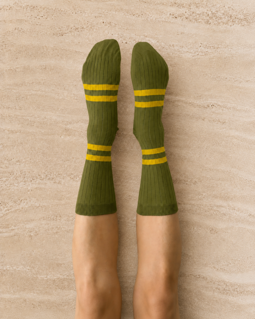 Escuyer Green socks with yellow stripes worn by a person on a stonebackground