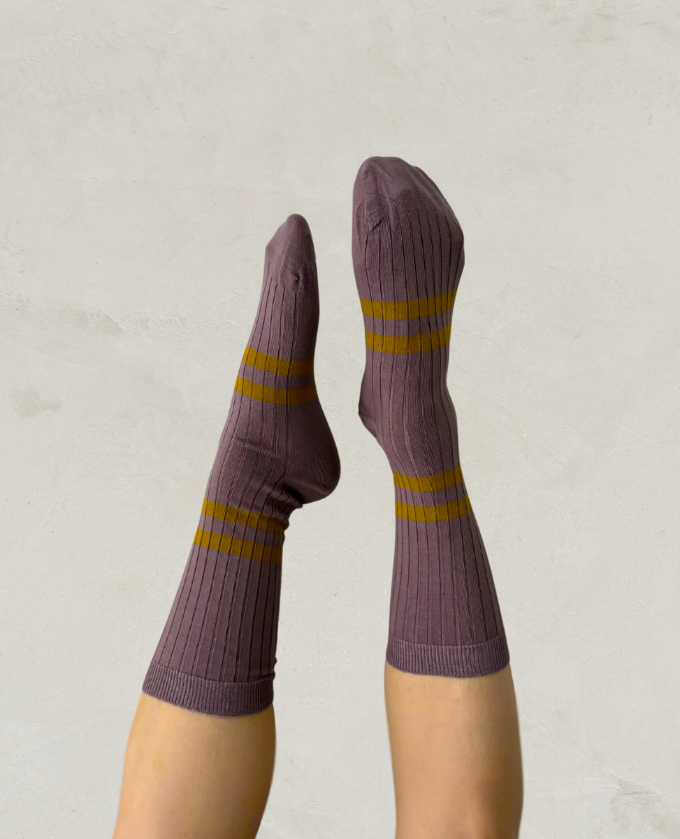 Escuyer Purple socks with yellow stripes worn by a person on a light gray background