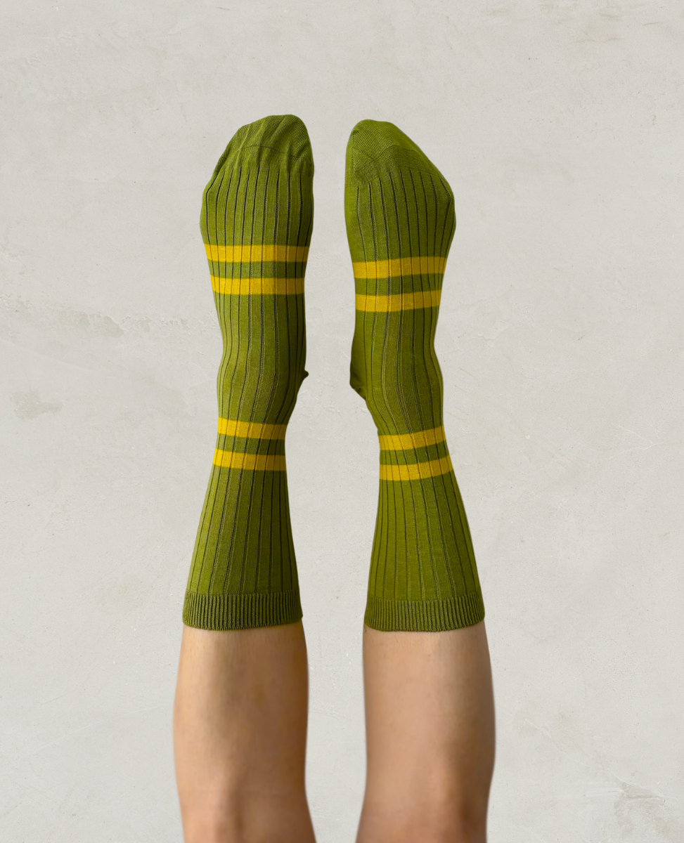 Escuyer Green socks with yellow stripes worn by a person on a light gray background