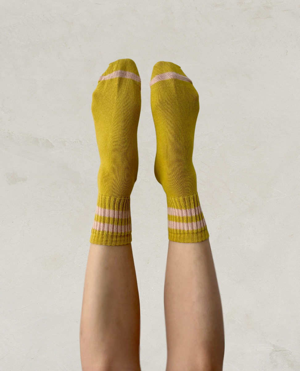 Escuyer Yellow socks with pink stripes worn by a person on a light gray background