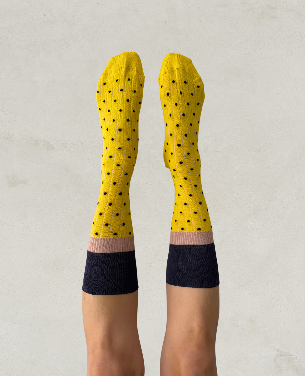 Exquisite J Yellow socks with black polka dots and pink and blue accents on a light gray background