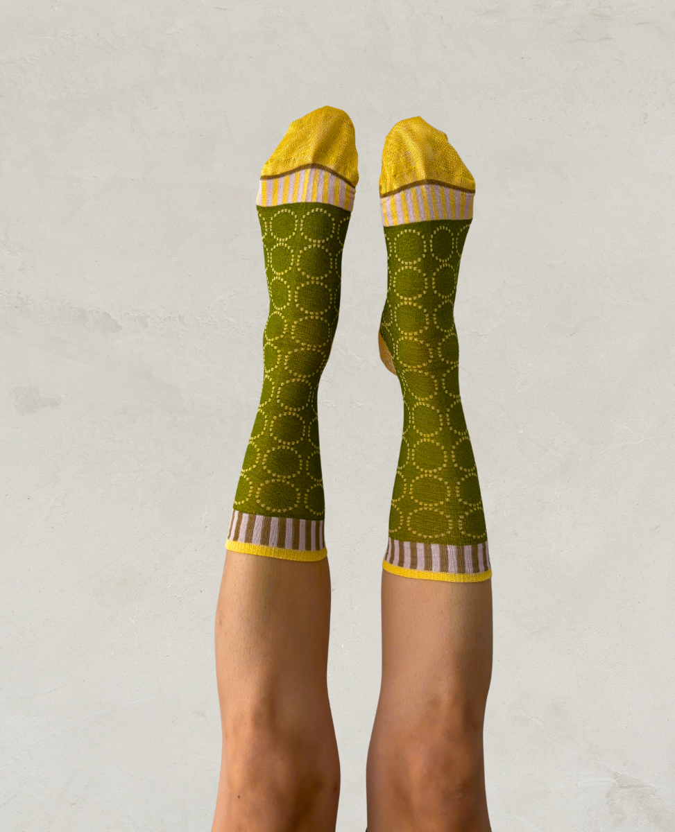 Exquisite J Green socks with yellow and white pattern worn by a person on a light gray background