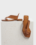 Brown leather sandals with a minimalist design feature a thong strap and a square toe, resting on a textured white surface. 1