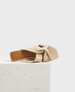 A beige, square-toed slide sandal with a twisted, soft leather upper and a flat sole, featuring a minimalist design and a subtle logo on the insole. 2