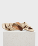 Beige sandals with a twisted strap design, featuring a square toe and flat sole, crafted from smooth, soft material. 1