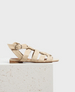 A beige gladiator sandal with multiple wide leather straps, a small buckle on the side, a flat sole, and a minimalist design. 1