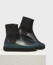 Sleek black leather ankle boots with a smooth finish, featuring elastic side panels, a teal rubber midsole, and a chunky black treaded sole. 1