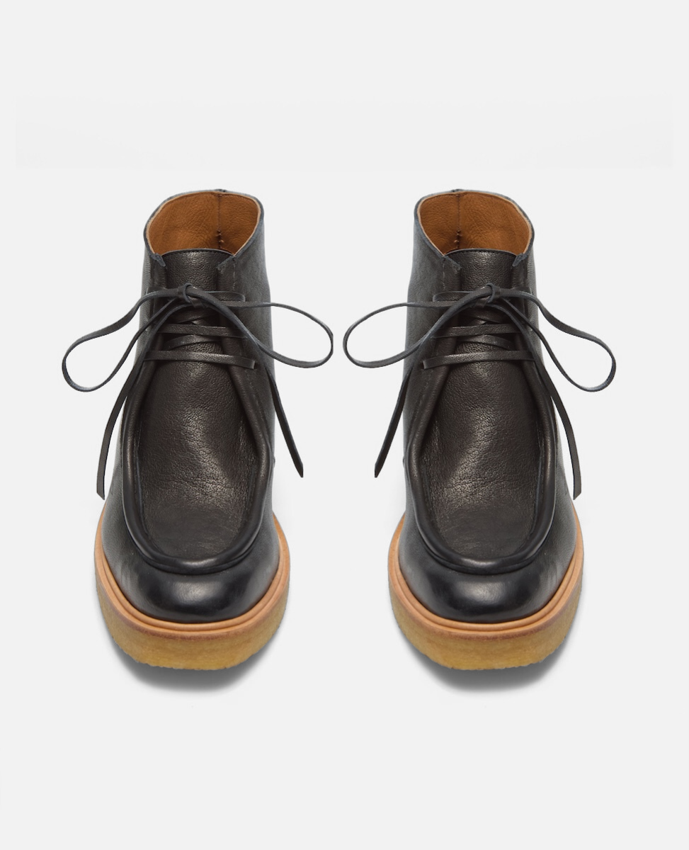 Pair of black leather boots with brown soles on a light gray background