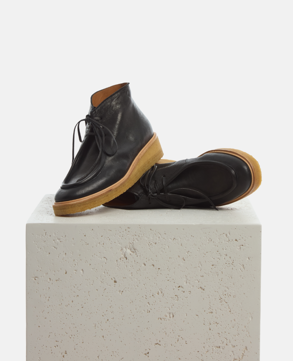 Pair of black leather shoes with brown soles on a light gray pedestal