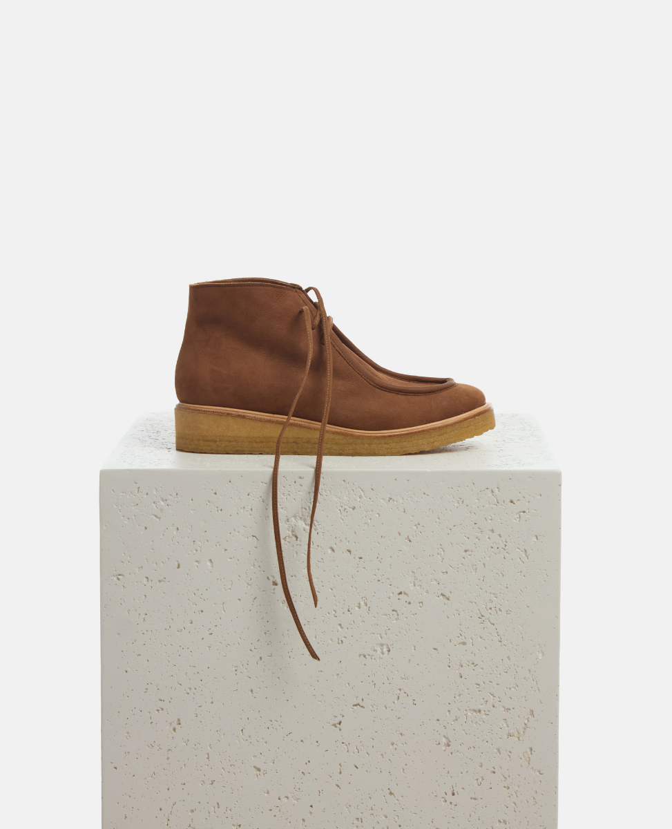 Brown suede shoe on a light gray pedestal against a white background