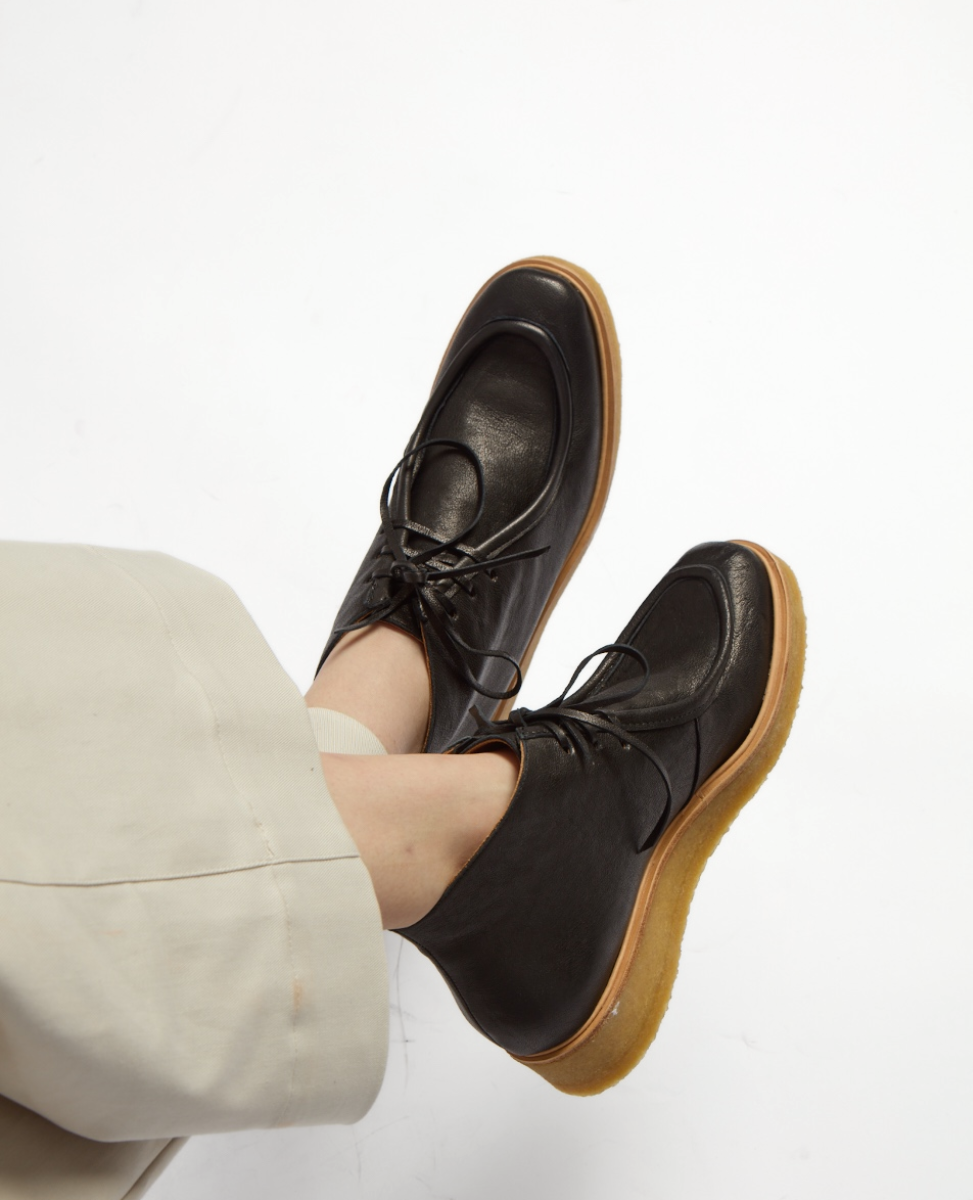 Black leather ankle boots with a smooth texture, round toe, and tan crepe soles, featuring lace-up fronts and a slightly elevated heel.