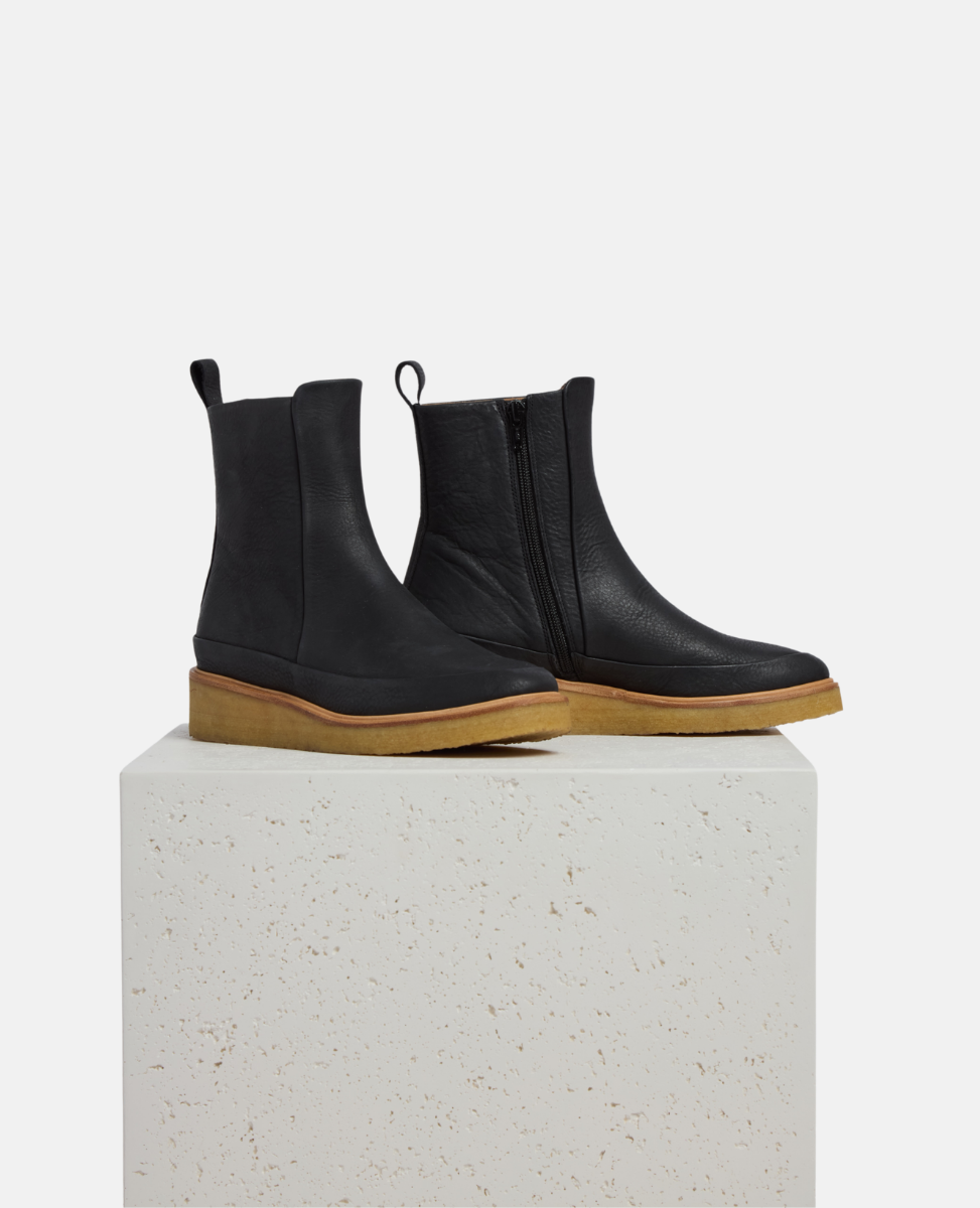 Black Chelsea boots with brown soles on a white pedestal