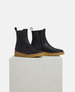 Black Chelsea boots with brown soles on a white pedestal 4