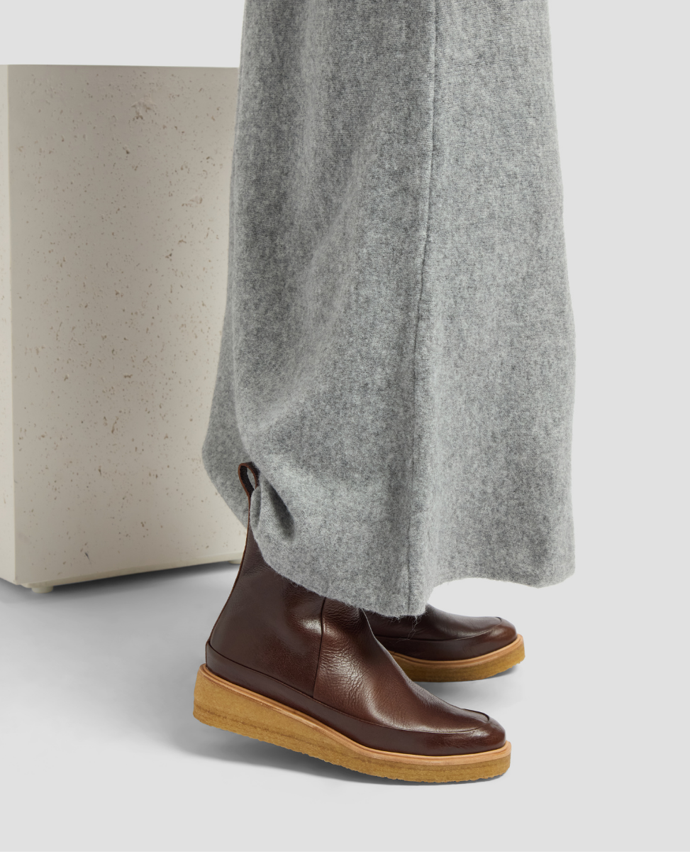 Brown leather boots with tan soles worn with gray pants on a light background