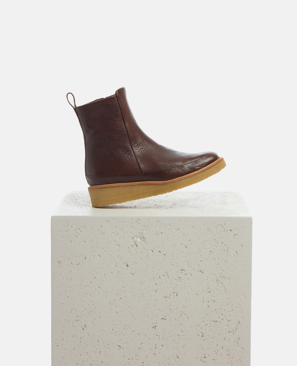 Brown leather ankle boot on a white pedestal with a light gray background