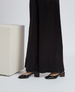 Black, wide-leg pants made of a smooth, flowing fabric paired with shiny black patent leather shoes featuring a low, block heel. 5