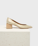 A gold, metallic-textured pump with a sleek, pointed toe and a distinctive wooden block heel, resting on a textured white surface. 1