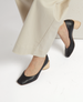 A pair of black leather shoes with a square toe and a light wooden block heel, worn with beige pants. 3