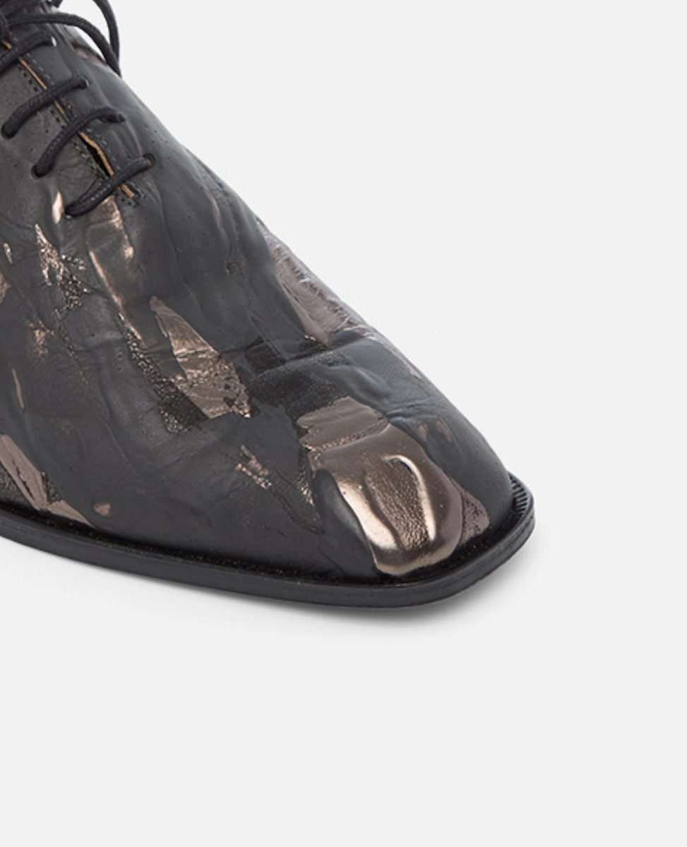 Black leather shoe with metallic accents on a light gray background