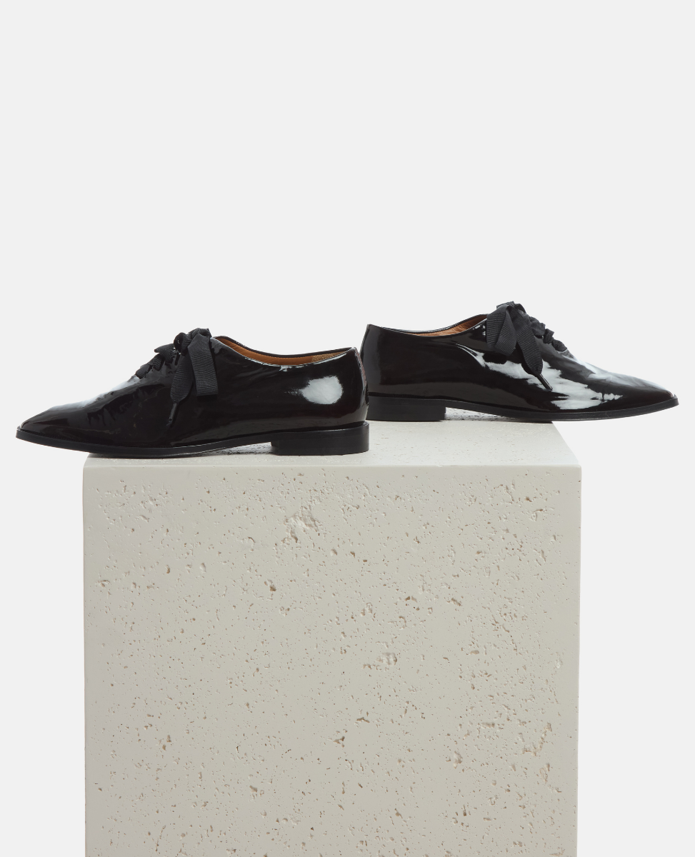 Black patent leather shoes on a light gray pedestal against a white background