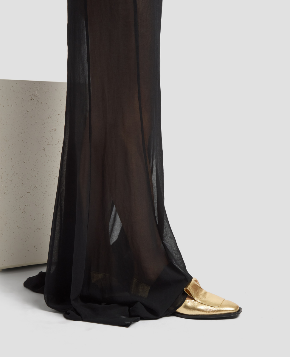 Black sheer pants with gold shoes on a light gray background