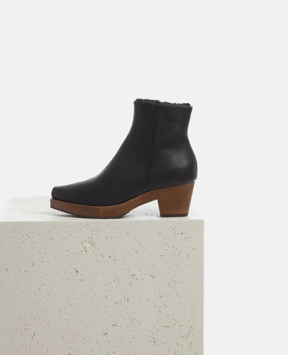 Black ankle boot with brown sole on a light gray surface