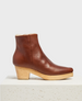 A brown leather ankle clog boot with a smooth texture, featuring a snip toe, a side zipper, a light wooden block heel, and a shearling, cream-colored inner lining. 1