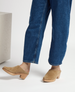 Tan suede clogs with a wooden block heel, featuring a closed toe and a smooth, minimalist design, worn with blue denim jeans. 2