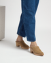 Tan suede mules with a closed toe, wooden block heel, and a smooth, minimalist design, worn with blue denim jeans. 5