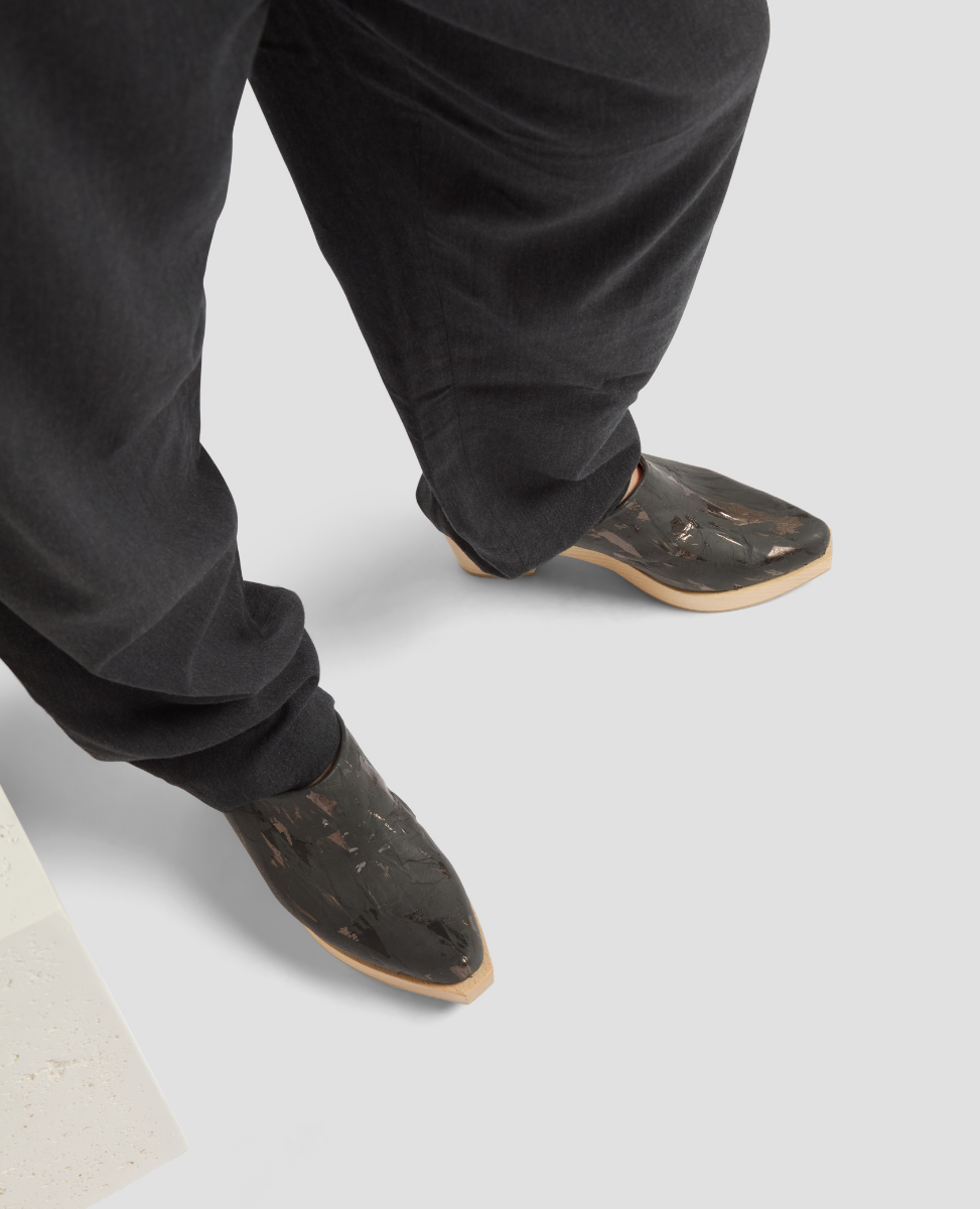 Person wearing black pants and brown shoes on a light gray background