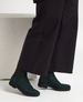 Dark teal suede ankle boots with a smooth texture, featuring black elastic side panels and a low black sole, worn with black wide-leg pants. 4